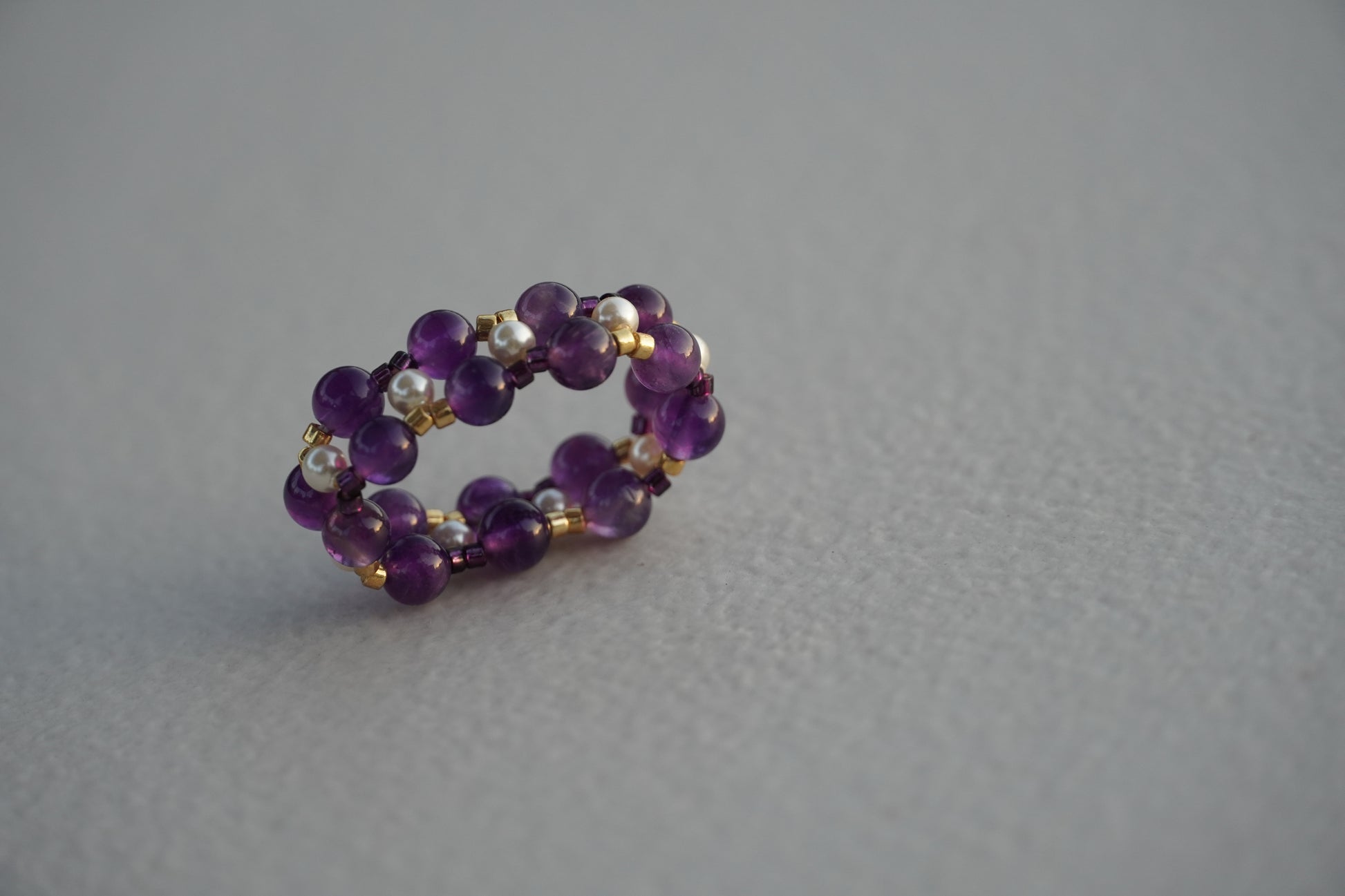 Purple beaded ring with gold accents on a gray background
