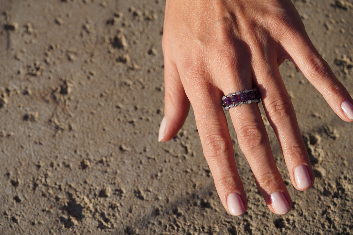 Hand wearing a ring with a purple gemstone on a textured surface
