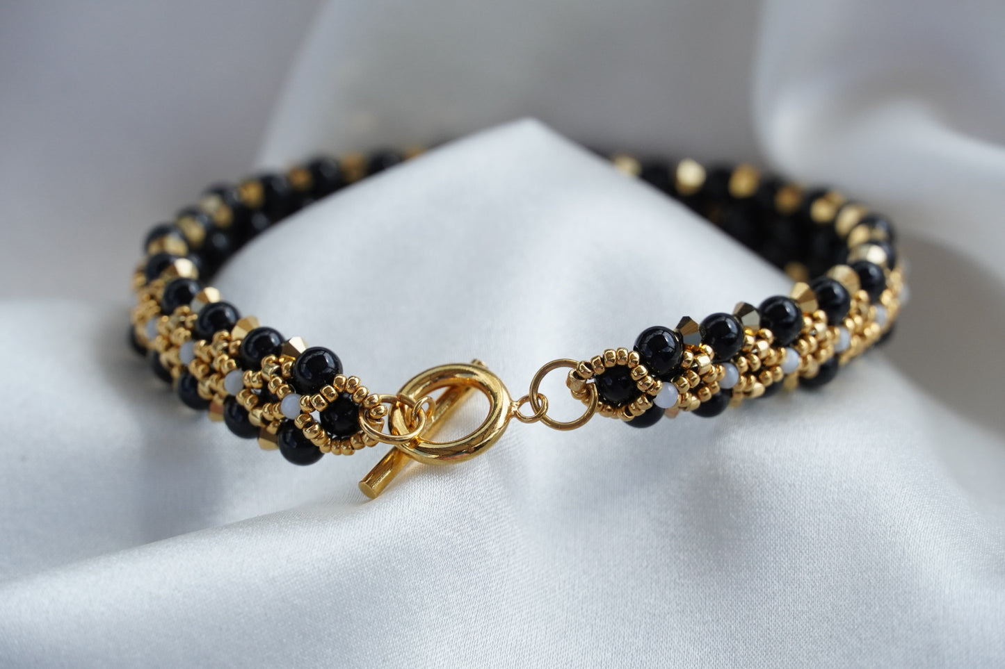 Gold and black beaded bracelet on a white fabric background