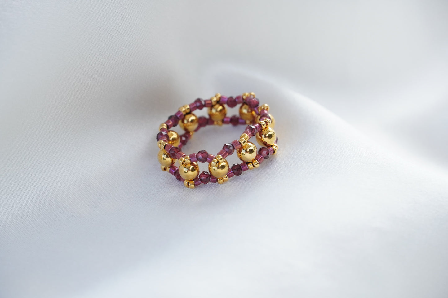 Gold and purple beaded bracelet on a white satin background