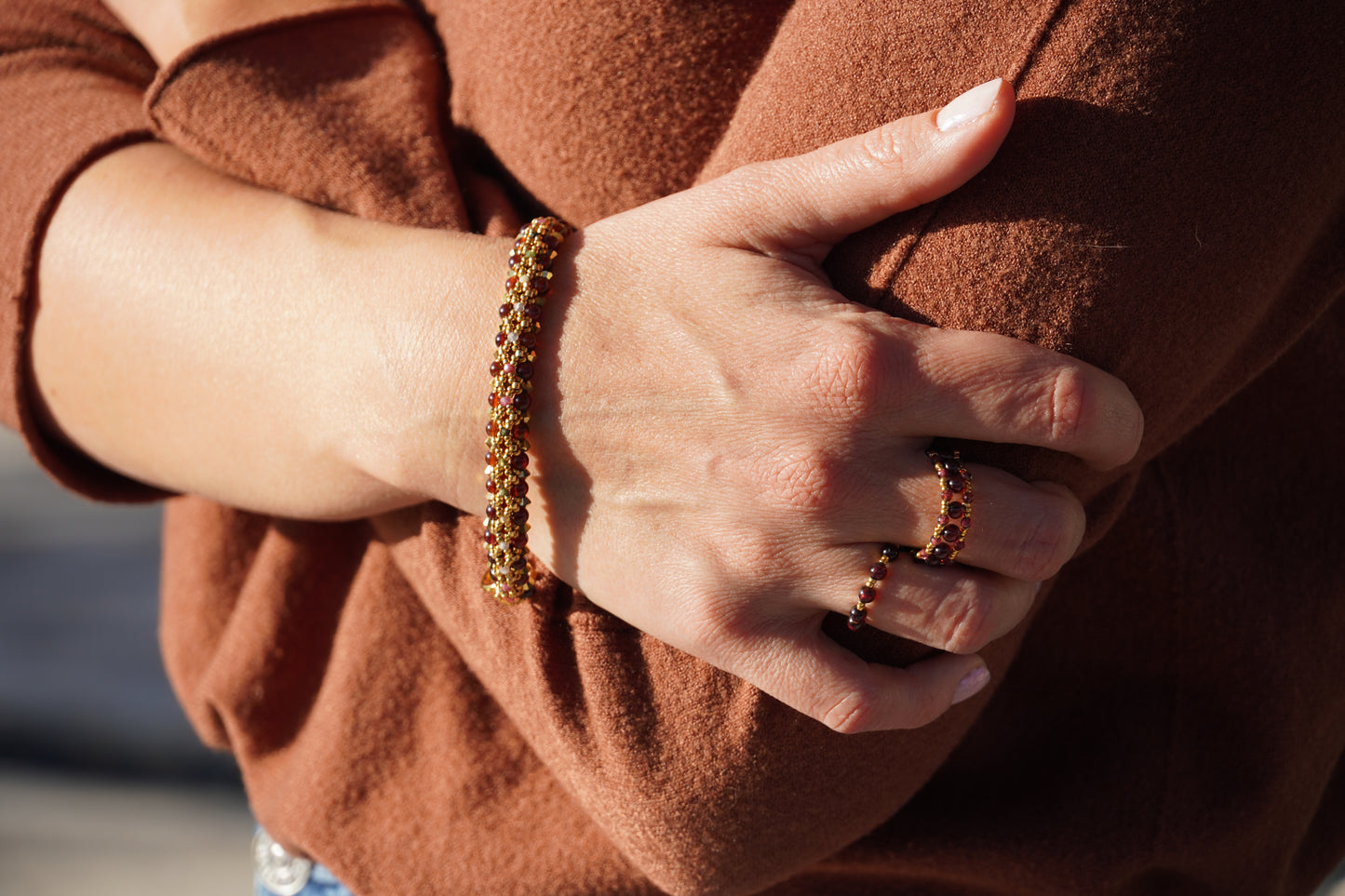 Close-up of a person wearing a gold bracelet and ring, holding a brown garment.