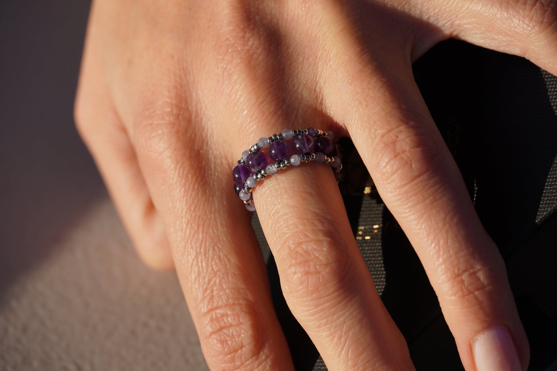 Close-up of a hand wearing a ring with amethyst and tanzanite gemstones.