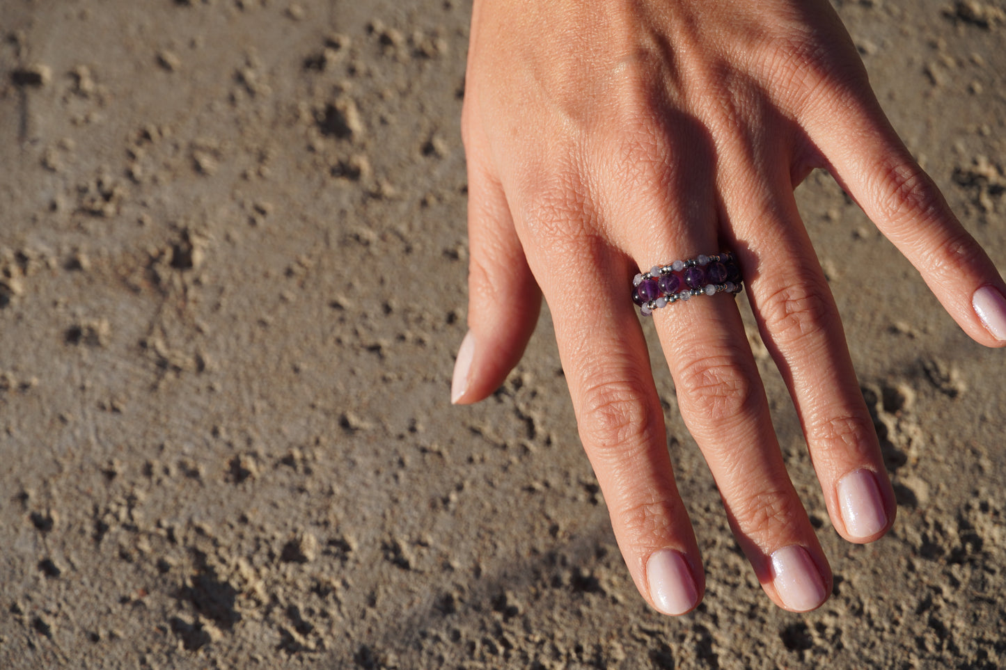 Hand wearing a ring with a purple gemstone on a textured surface