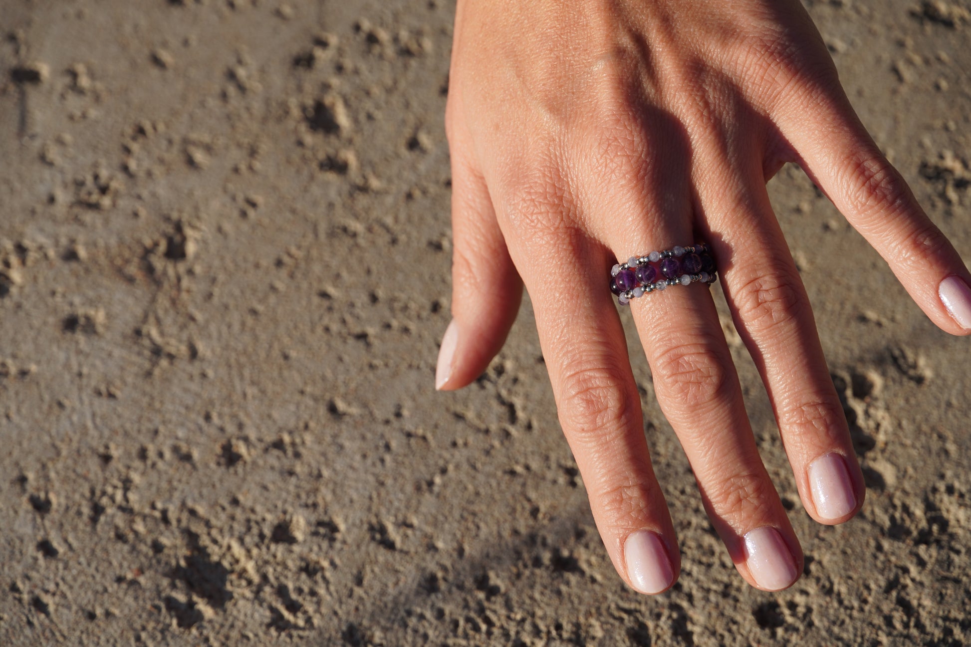 Hand wearing a ring with a purple gemstone on a textured surface