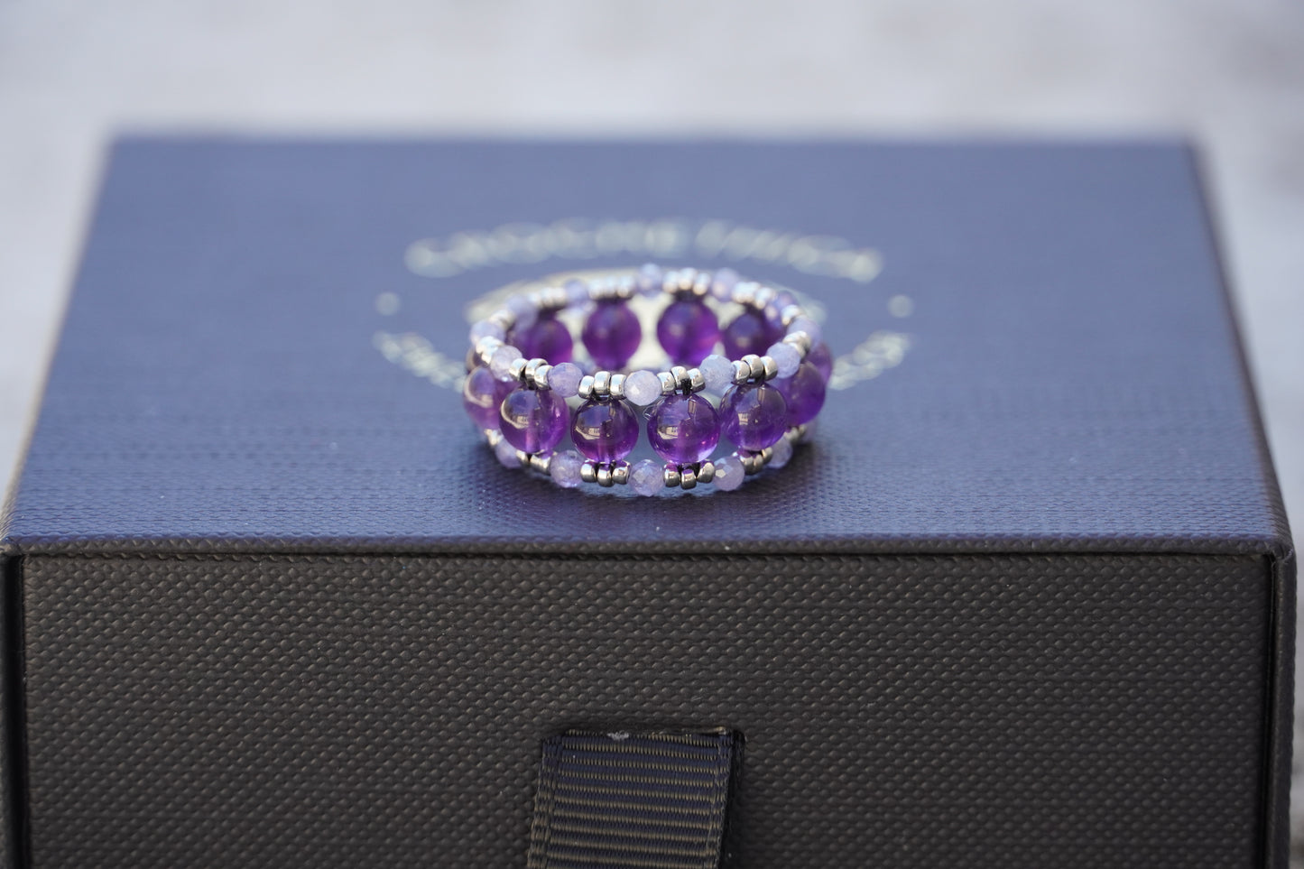 Amethyst beaded ring on a black box with a visible brand name.