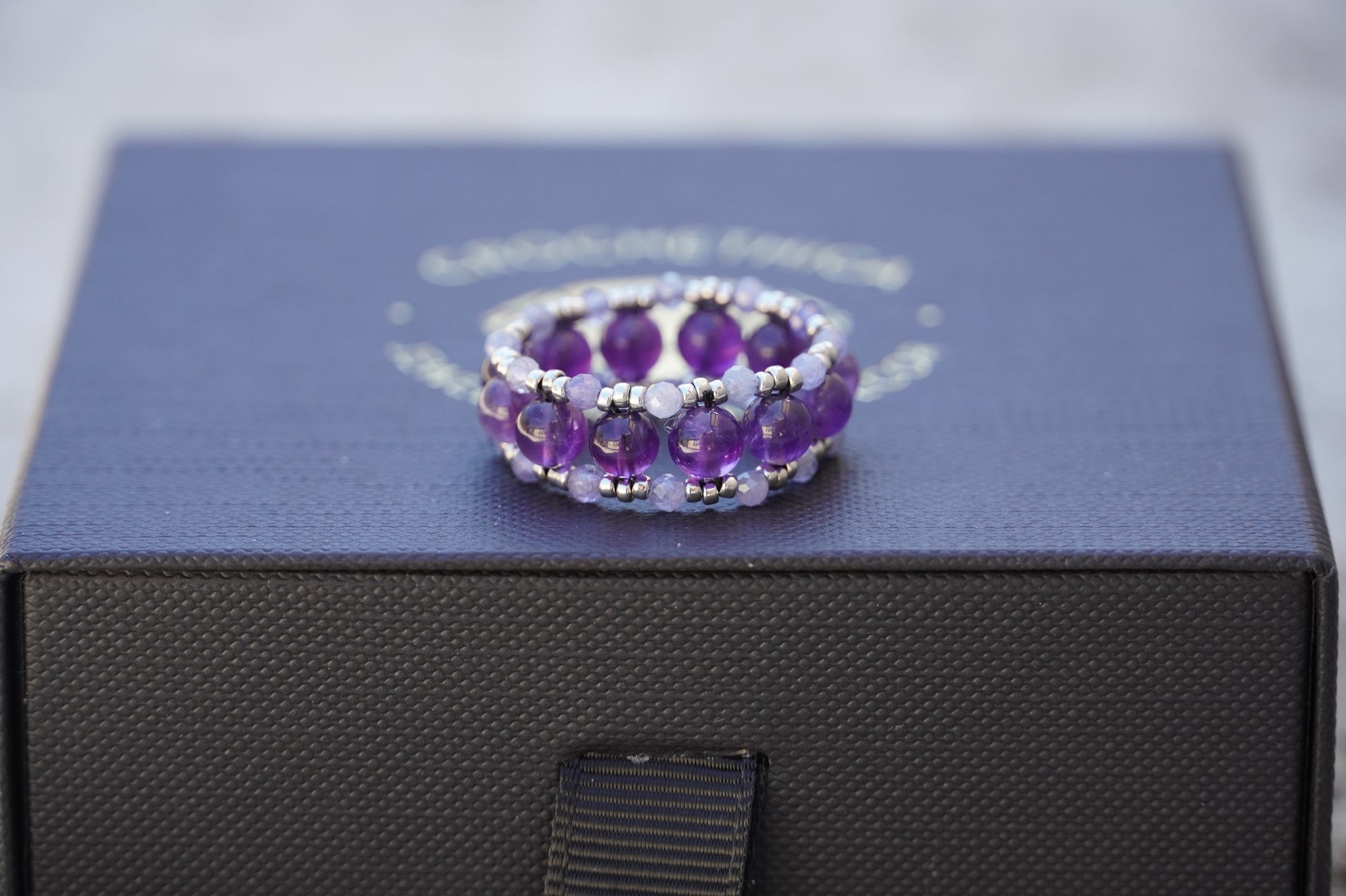 Amethyst beaded ring on a black box with a visible brand name.