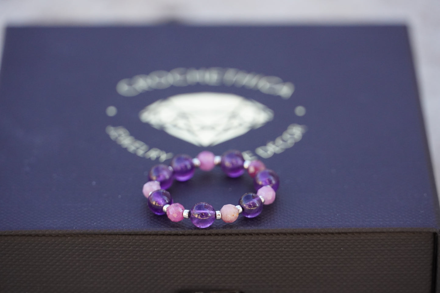 Purple beaded ring on a jewelry box with a visible brand logo.