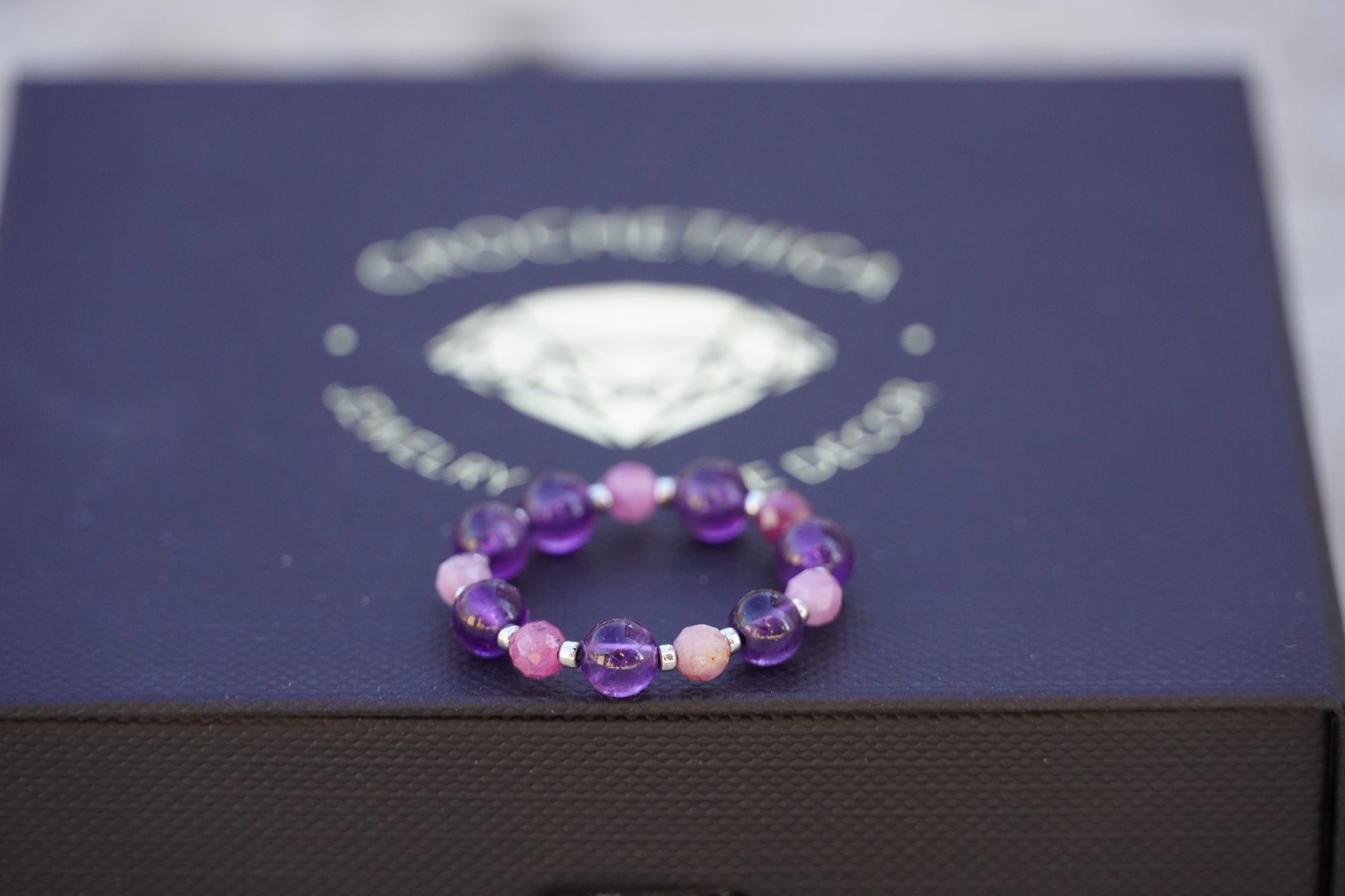 Purple beaded ring on a jewelry box with a visible brand logo.