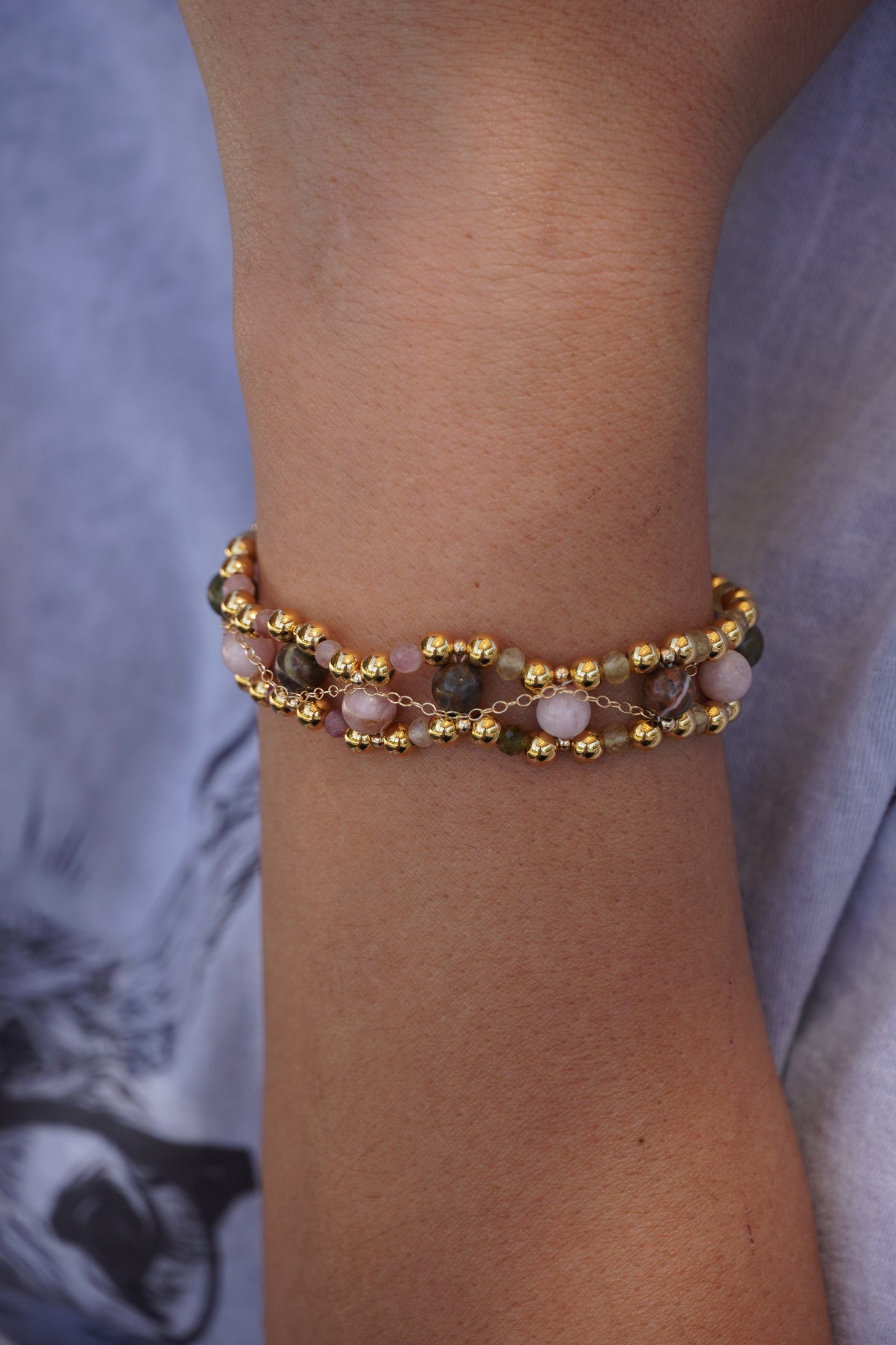 Close-up of a wrist wearing a gold beaded bracelet against a blurred background