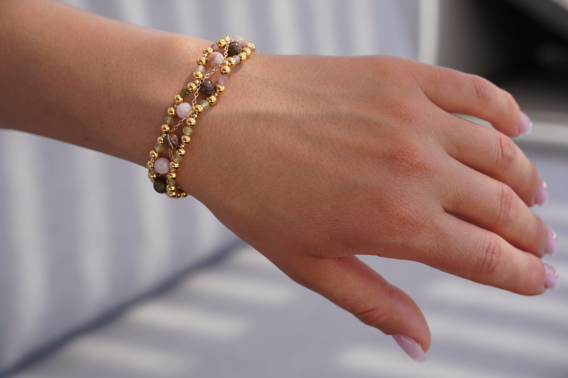 Hand wearing a gold bracelet with pink beads on a blurred background