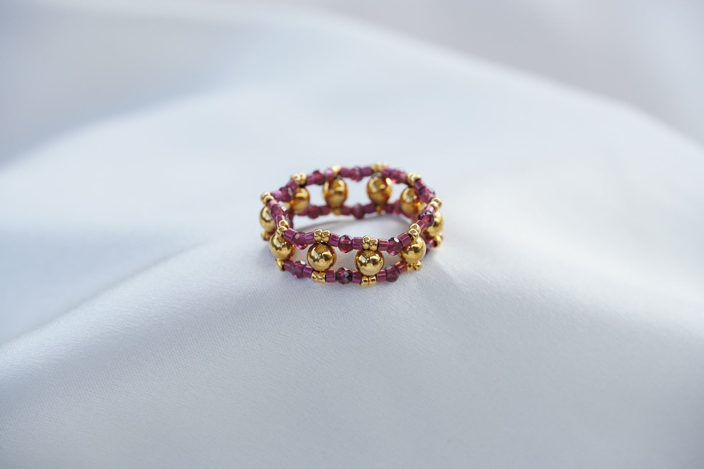 Beaded bracelet, gold and purple, on a light gray surface.