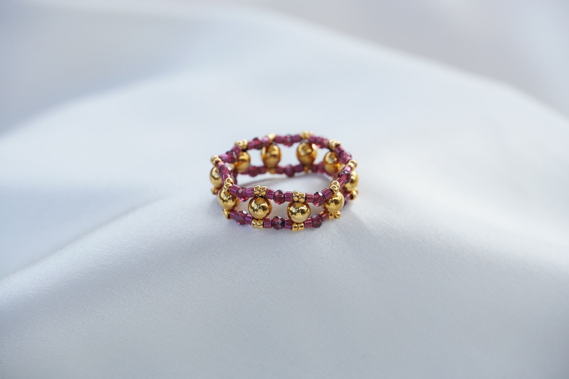 Beaded bracelet, gold and purple, on a light gray surface.