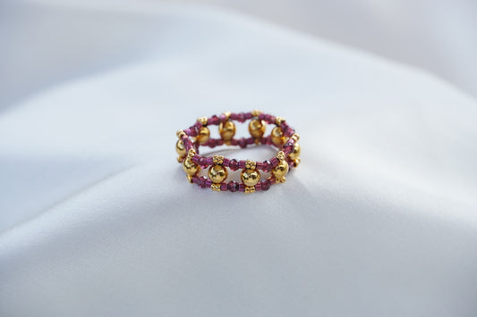Beaded bracelet, gold and purple, on a light gray surface.