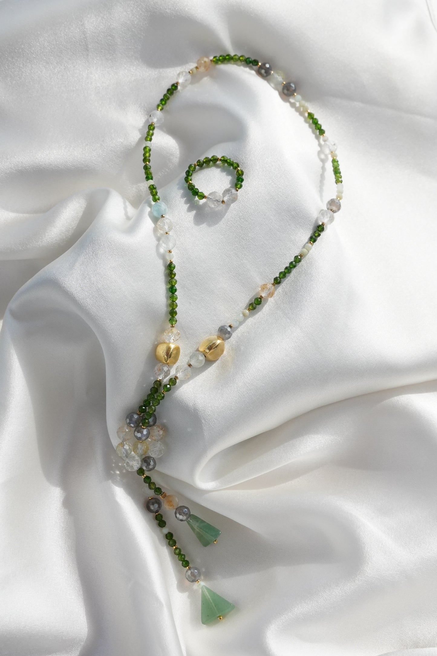 Beaded necklace with green and gold elements on a white fabric background