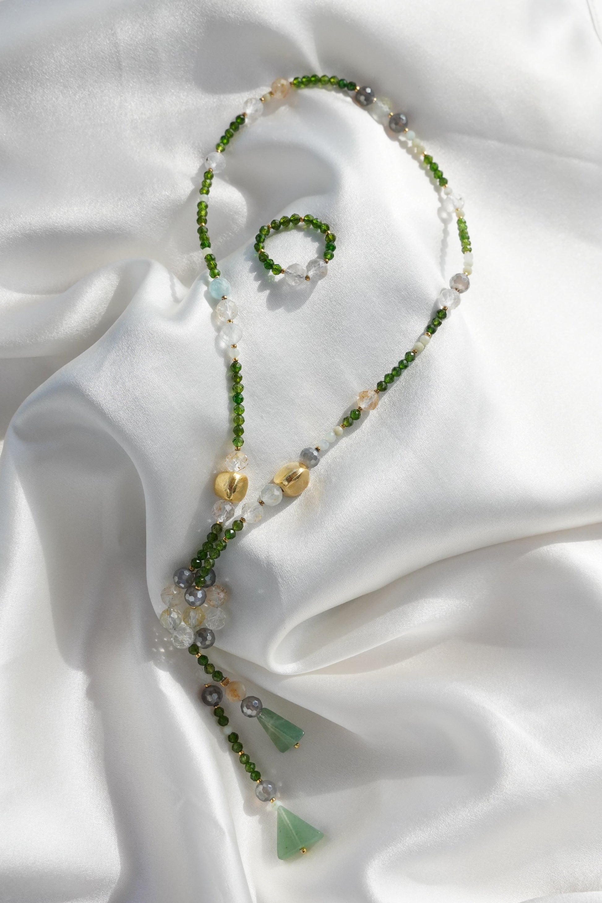 Beaded necklace with green and gold elements on a white fabric background