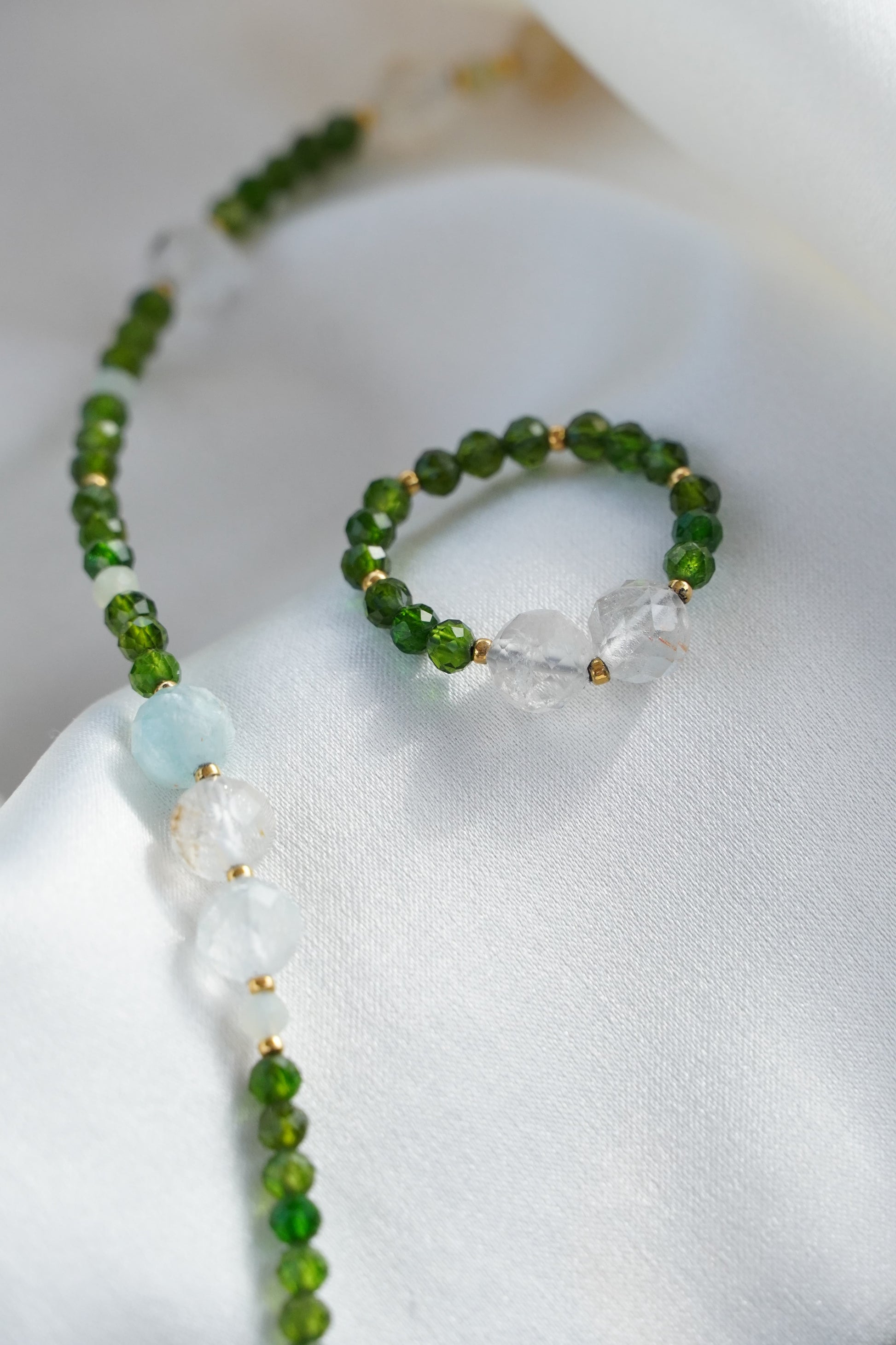 Beaded necklace and ring with green and clear beads on a white surface