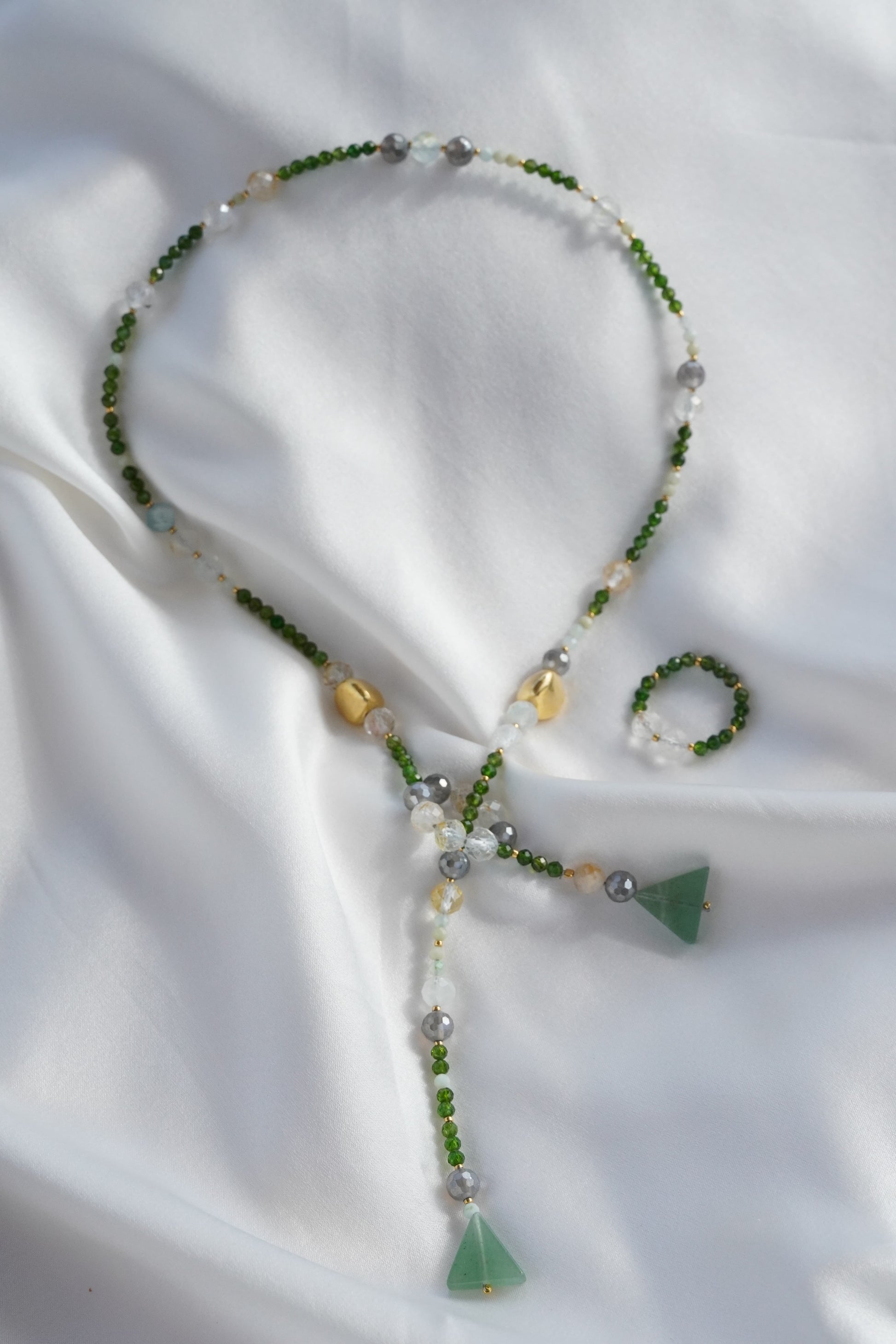 Beaded necklace with green triangle pendants on a white fabric background