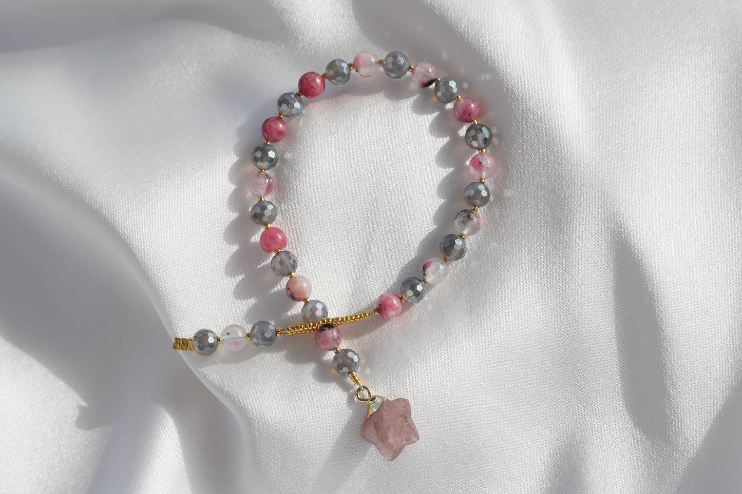 Beaded bracelet with pink and gray stones on a white fabric background