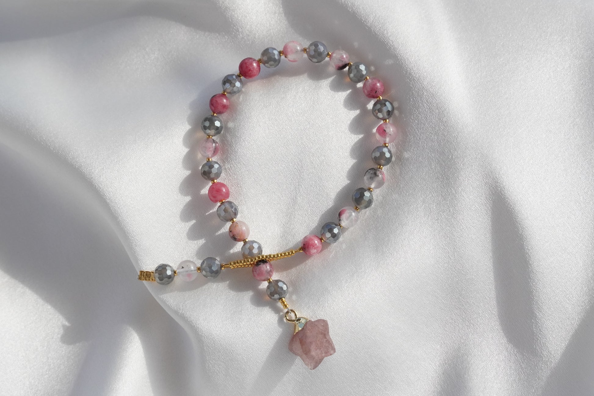 Beaded bracelet with pink and gray stones on a white fabric background